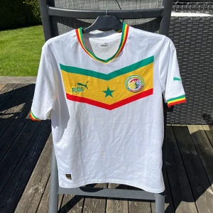 Senegal 22/23 Fotbollströja - Säljer av en hel del fotbollströjor, denna Senegal tröjan har använts en 3-4 ggr. Finns en fläck på framsidan (se sista bilden), men syns knappt. Inte original! Storlek: M Skick: 8.5/10