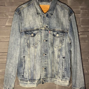 Blå jeansjacka - En klassisk blå jeansjacka från Levi's med knappar framtill och två bröstfickor med knappstängning. Jackan har en normal passform och är tillverkad i slitstarkt denimtyg. Endast använd en gång, nyskick! Nypris 1200