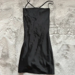 Svart satin klänning - Svart satin miniklänning från H&M,använd 1-2 gånger kanske. Super fint skick och super fin,säljer för att jag inte gillar hur den sitter på just mig men annars älskar jag den. Normal i storleken,inga fel eller defekter på den. Öppen rygg med snörning