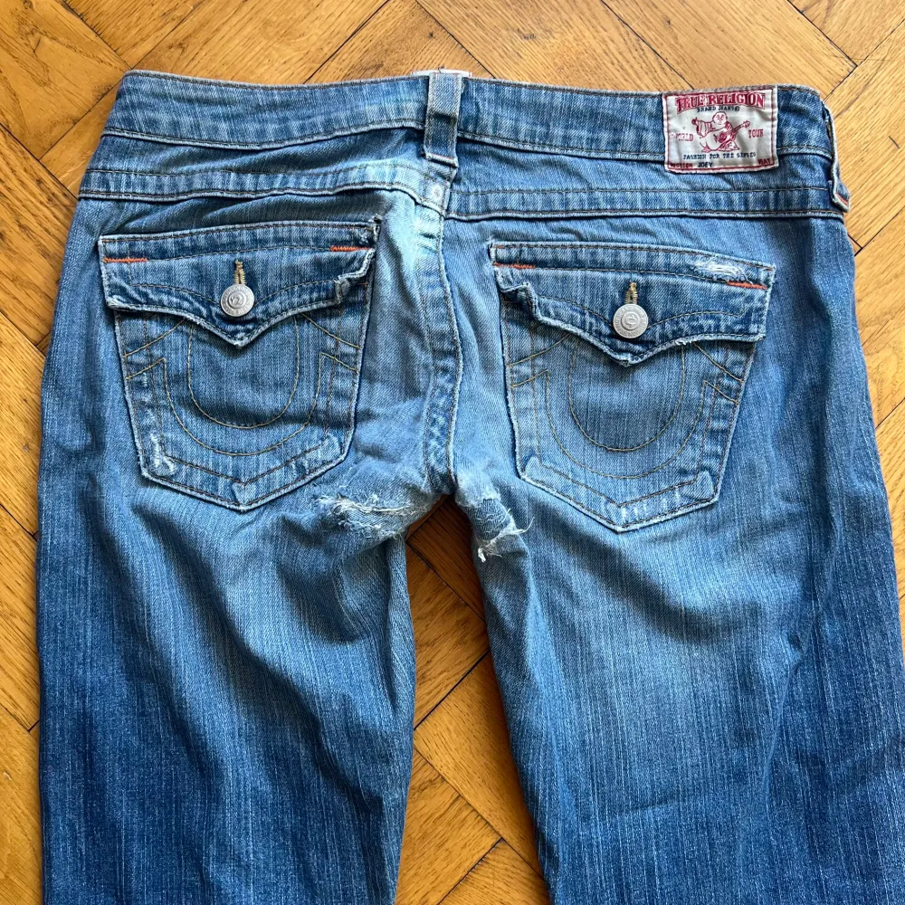 Lågmidjade True Religion jeans i modellen bootcut. Har defekter (se sista sliden), hål under rumpan som blivit ihoplappade (fortfarande små hål), två hål vid fickorna och slitage längst ner. Mått i cm: midja: 42, Innerben: 79. Jag är 165 ❤️. Jeans & Byxor.