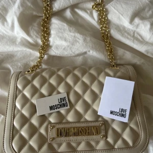 Love Moschino väska - Säljer nu min fina beigea Love Moschino som tyvärr inte kommer till användning för mig längre. Köpt på Zalando för ca 3000kr. Använd fåtal gånger.🤍 Måtten är 26 x 18 x 8 cm🥰