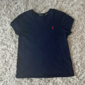 Blå Ralph Lauren t-shirt  - Blå t-shirt ifrån Ralph Lauren med en röd Ralph Lauren märke på. T- shirten är i nyskick då den aldrig är använd. Köptes för 899 säljer därför för ganska mycket men priset är förhandlingsbart vid snabba affärer!