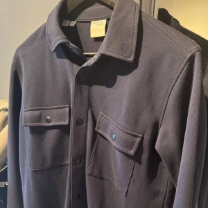 Overshirt - En riktigt stilren Overshirt från Selected Homme i storlek ”S”. Overshirten är marinblå och är bara använd ett fåtal gånger. Du kan matcha den med nästan vad som helst under, allt från en skjorta, en t-shirt till en lite tjockare tröja osv. 