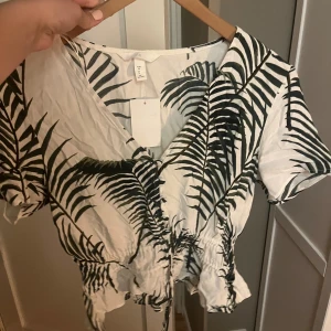 H&M blus - Vit blus med palmblad. Sitter bra. Helt oanvänd med prislappen kvar! Köpt för 199kr.