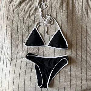 Svart och vit bikini - En svart bikini med vita kanter. Överdelen har knytband runt nacken och ryggen, och underdelen är en klassisk bikiniunderdel. Aldrig använt, från NA-KD