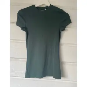 Slim Fitted T-shirt från Weekday i mörk grön färg. Tröjan är i nytt skick, har aldrig använts! Tröjan är i ribbat material och i storleken XS💫