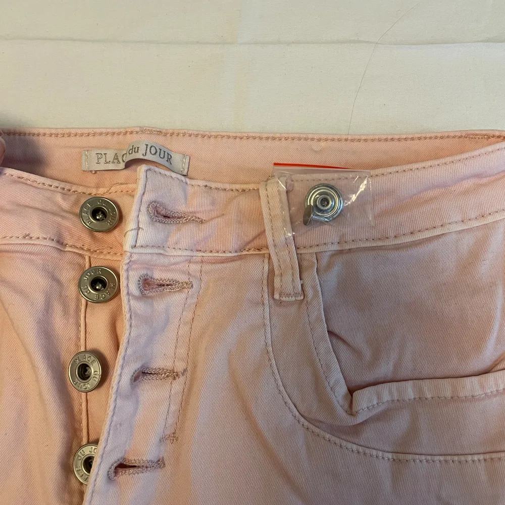Ljusrosa jeans från Place Du Jour. Jag har aldrig använt, prislapp sitter kvar. Knapparna går att knäppa upp och finns även reserv knap med, se sista bilden. . Jeans & Byxor.