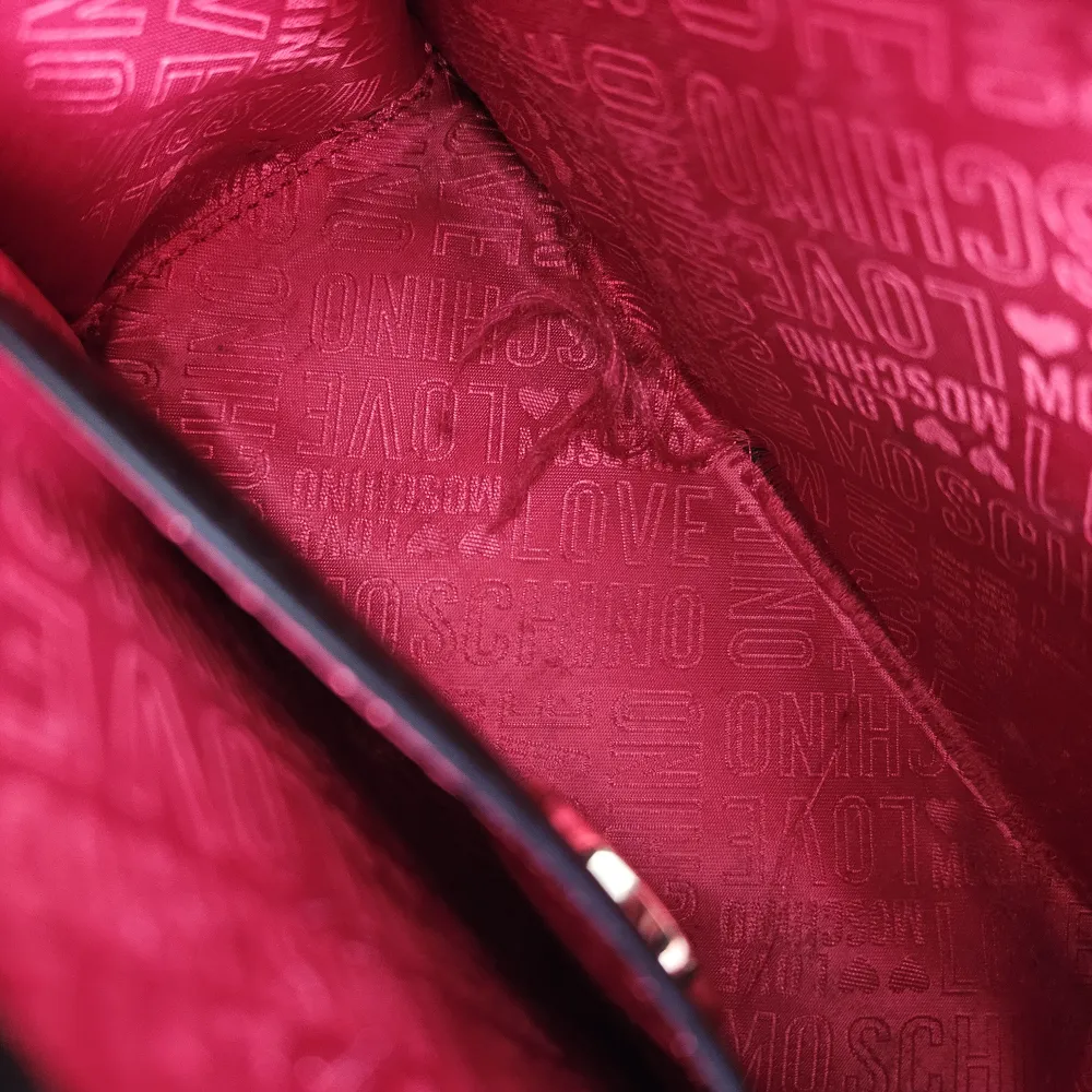 Axelremsväska i läderimitation från Love Moschino Dekorativ rosett som går att plocka av. Dustbag medföljer  Lätt skada på undersidan och även en söm som gått upp i väskan. . Väskor.