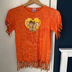 Orange t-shirt med koalor som kramas och pärlor fint dekorerade vid kanterna. Har aldrig använts och kommer från pi cottons