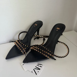 svarta klackskor med nitar - svarta klackskor från zara med guldiga nitar i storlek 37. nypris 699. aldrig använda med lapp kvar. 