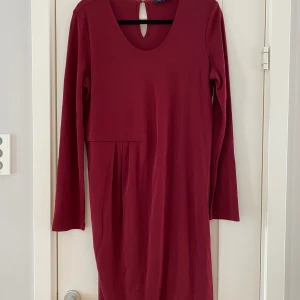 Ny mörkröd långärmad klänning från Tommy Hilfiger i strl M - Ny mörkröd långärmad klänning från Tommy Hilfiger i strl M.  Ny, aldrig använd.  Mått Över bröstet: 53 cm Längd från axeln och ner: ca 96 cm  70% viskos och 30% polyester 