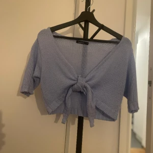 Stickad tröja med knytning fram blå ljusblå - Ljusblå stickad kort topp med knytning framtill. Storlek M. Använd enstaka gång.