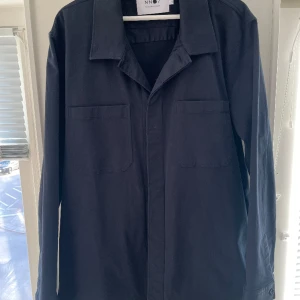 NN07 Overshirt Bernie 1420 - Overshirt från NN07 i färgen navy blue. Två bröstfickor samt en ficka på vardera sida vid magen. Använd ett fåtal gånger. Skick: 9/10 Nypris: 1999 kr