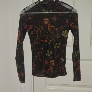 Svart genomskinlig tröja med blommor - Lång i längden. Bra skick men använd några gånger och lite sliten i en söm 