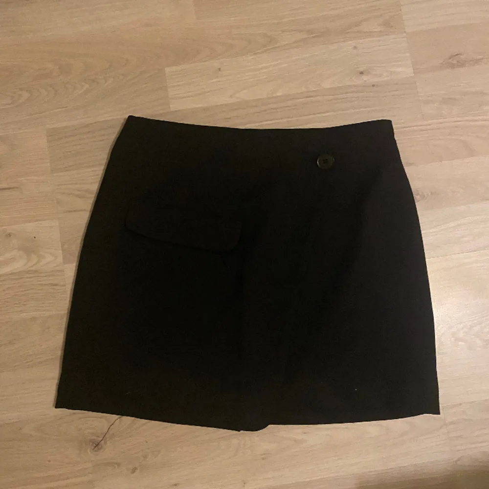 Fin svart kjol från H&M🌟Kjolen är kort och har en ficka och en knapp på framsidan. Säljer den då den ej kommer till använde. Kjolar.