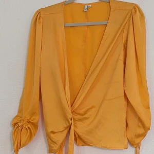 Gul omlottopp från NLY Trend - En gul omlottopp från NLY Trend med långa ärmar och knytning framtill. Toppen har en djup v-ringning och rynkade detaljer vid ärmsluten.