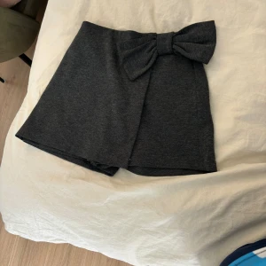 Grå kjol med rosett - En kort grå kjol med en stor rosett framtill. Kjolen har en enkel och elegant design. De är shorts 💕 även stor i storleken 