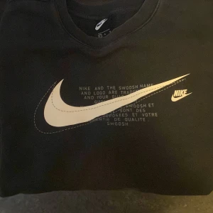 Svart tröja från Nike - En svart tröja från Nike med en stor vit Nike-logga och text på framsidan. Den är väldigt skönt och varmt. Den är i bra skick. 