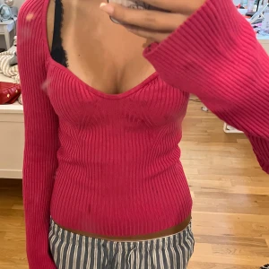 Röd ribbad tröja - En rosa ribbad tröja med långärmade ärmar. Tröjan har en tight passform och en djup v-ringning.