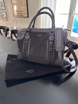 Zadig Voltaire Sunny väska medium  - Säljer min Zadig Voltaire Sunny väska i storleken medium. Väskan är grå i mocka med skin detaljer samt metall detaljer. Prislappen och dustbag finns, tyvärr inget kvitto då det var en present, nyköpt i Köpenhamn.