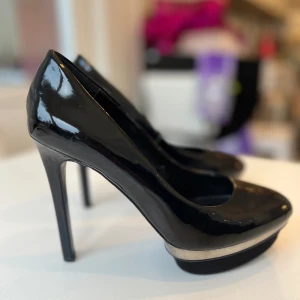 Svarta höga klackar - Supersnygga svarta lackpumps med detaljer i silver och fejkmocka. Smal hög klack (12,5 cm) och hög platå (3 cm). Säljer p g a de är för små för mig. Passar 38, 38 1/2 eller liten 39. 