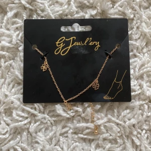 Fotlänk från GJ Jewellery - En snygg fotlänk i guld från GJ Jewellery. Fotlänken har små dekorativa hängsmycken i form av blommor och är justerbar i längd. Helt ny.🥰