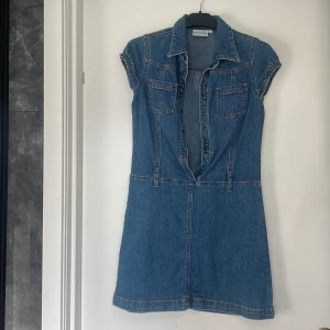 Jeansklänning från Check This by Lindex Girls - En stilren jeansklänning från Check This by Lindex Girls i storlek 152. Klänningen har korta ärmar, två bröstfickor och knappar framtill. Den är tillverkad i ett klassiskt blått jeansmaterial och har en figurnära passform.