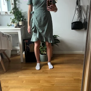 Omlott klänning  - Grön omlott klänning med svarat blommor på från ONLY. Köpte klänningen secondhand men har själv aldrig använt den