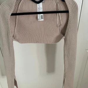 Ribbstickad bolero - Ribbstickat beige bolero med slits vid armarna från Chiquella. Storlek S. Nyskick, helt oanvänd.