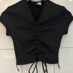 Kortärmad tröja - Jag säljer denna fina kortärmade toppen i svart. Den är använd 1-2 gånger så alltså i väldigt bra skick. Den går att justera själv med snörena. Kontakta för mer info eller bilder på den 🫶