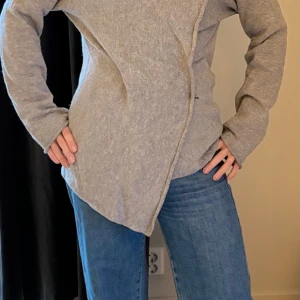 Hunkydory kofta essential Japan knit slätstickad ullmix - Hunkydorys klassiska cardigan i ljusgrå. Essential Japan Knit rakt skuren omlottmodell med hakar på insidan som kan bäras som man önskar. Längd 54cm i strlk M. 20% alpacka, 70% lammull, 10% polyamid.