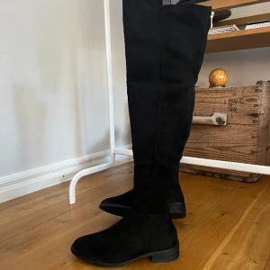 Höga stövlar mocka-imitation Nyskick  - Höga svarta stövlar i mockaimitation med guldkedja, snygg modell med tajt siluett. (Dolt blixtlås på sidan, inåt. Ny snygga men används inte. Hoppas någon annan kan få glädje av dem. 