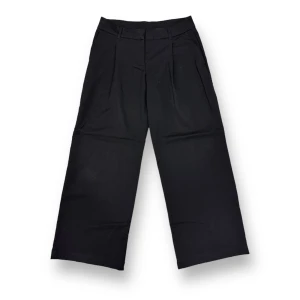 Skräddade byxor med låg midja och vida ben - Ett par skräddade byxor med låg midja och vida ben med veck fram, dragkedja med hyska och hake samt sneda sidofickor.   Lös passform. Låg midja. Sneda sidofickor. En påsydd ficka bak. Hällor. Tillverkade i återvunnen polyester.