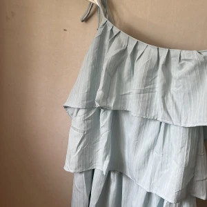 Blå klänning med ett band på axeln  - Blå klänning med ett band, klänningen är aldrig använd,  volang klänning, jätte fin inför sommaren, fler bilder skickas vid önskemål, storlek 38