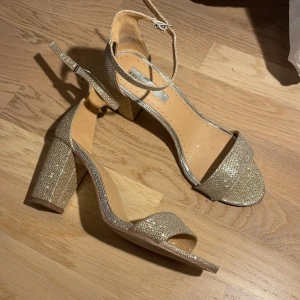 Glittriga Klackskor  - Glittriga klackskor med öppen tå. Som har blivit använda en gång.   Klackskorna är storleken 39. Klacken är 8 cm hög.