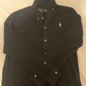Svart Polo Ralph Lauren skjorta - Featherweight mesh material: Sitter lite löst och passar alla storlekar beroende på ens egna kroppsbygg. Prisen är inte satt i sten och hör av er för fler frågor.