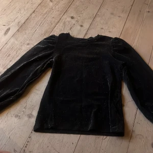 Glittrig festtopp  - Svart glittrig festtopp, perfekt på nyår. Köpt för ca 400-500 kr, säljer för billigt. Toppen är långärmad, puffig på axlarna och vid handlederna. Storlek: XXS-XS/13-14 år. Inga defekter. ❤️KOLLA MIN PROFIL RENSAR UT GARDEROBEN!!!