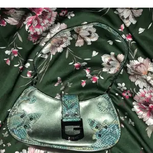 En äkta guess väska i grön färg, den har läder med kamouflage färg 