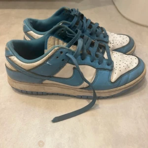Nike Dunk Low UNC - Använda en del, skulle bedöma skicket som 5,5/10 i en skala där en 10 är som nyköpta. Har slitage invändigt men utvändigt är dom rätt fräscha. Dessa skor är som en aktier och går upp o ner i pris hela tiden. Just nu värderas dom som nypris till ca 6000kr 