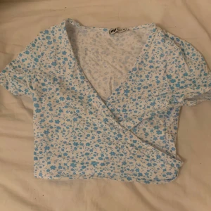 Vit tröja med blå blommor - Den här tröjan har varit använd endast två gånger och är perfekt för dig som ska på en resa i ett härligt soligt klimat!