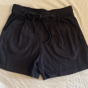 Svarta shorts med knytband - Ett par svarta shorts med knytband i midjan och ett par mörkblåa shorts. Shortsen har fickor på sidorna och är tillverkade i ett mjukt material.
