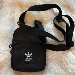 Adidas axelväska  - En svart Adidasväska i bra skick. Man kan typ ha mobilen och plånboken och passar att ha med sig i alla tillfällen. Skriv om intresserad💗