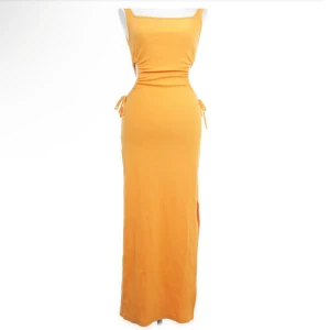 Långklänning med utskärningar - En elegant långklänning med utskärningar på sidorna och knytband. Klänningen finns i två färger: orange och blå samt i grön. färgerna är mer färgade i verkligheten. Den har en tight passform och är ärmlös. Pris: 200kr/st