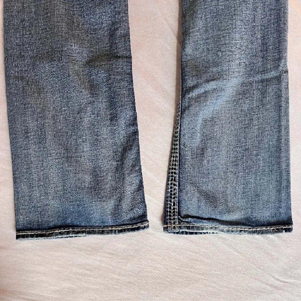 Rock Revival bootcut jeans. Vita designstygn både fram och bak med kristallnitar. Bra skick på tyget men lite nitar som lossnat och framknappen har en spricka (enligt bilderna). Nypris: Rock Revival bootcut ca 1900kr. Hör gärna av dig om du har frågo. Jeans & Byxor.