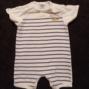 Randig playsuit/jumpsuit strl. 62 - Vit playsuit/jumpsuit/onesie med blå ränder i strl. 62. I okej begagnat skick, blekare än ny samt något "tvättluddig" men fungerar fint för fler barn. En liten dov fläck finns på baksidan.  Tvättad i parfymfritt tvättmedel och utan sköljmedel.