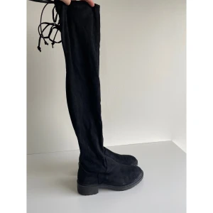 Overknee-stövlar - Svarta stövlar som går upp över knäna från New Look (Zalando) i strl 36. Mockaliknande material och snöre bak. Klackhöjd ca 3 cm och höjd från häl till knä ca 60 cm. I fint skick, använda fåtal gånger.  Kommer från djur- och rökfritt hem.