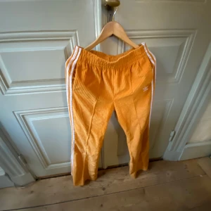 adidas byxor - adidas Originals – Orange utsvängda manchesterbyxor med tre ränder. US Medium  Använda ca fem gånger