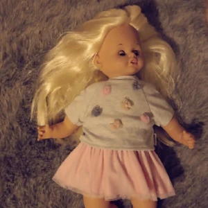 En skrollan docka - Med blont hår, blåa ögon och två aoutfits.