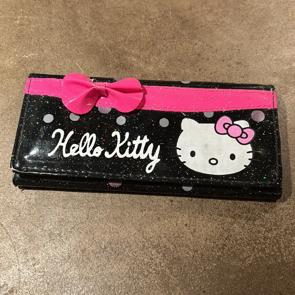 Glittrig plånbok med Hello Kitty-motiv. Söt rosa rosett. Fack för kort, mynt samt kvitton och pengar. Mått 18,5x9 cm. . Väskor.