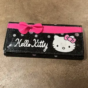 Glittrig plånbok med Hello Kitty-motiv. Söt rosa rosett. Fack för kort, mynt samt kvitton och pengar. Mått 18,5x9 cm. 